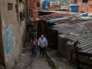 A man and a woman walk side by side up the staircase of a narrow street beside tin-roofed buildings 