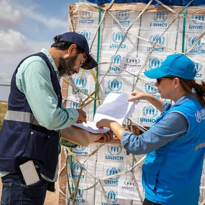 Two UNHCR staff members check a shipment of emergency supplies against a list