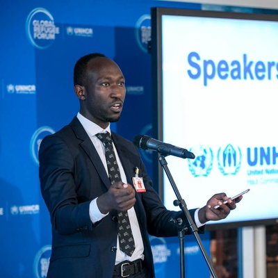 A man gives a speech, behind him a sign reads ' Speakers' Corner'