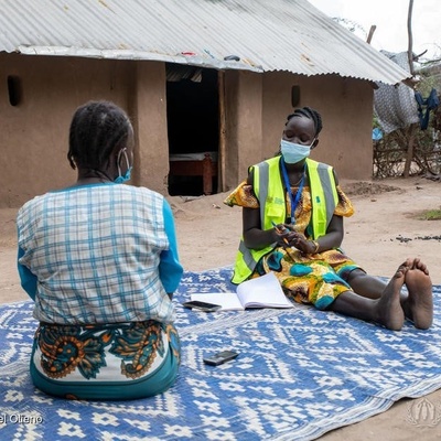 UNHCR partner sits on the floor and talks with a refugee woman