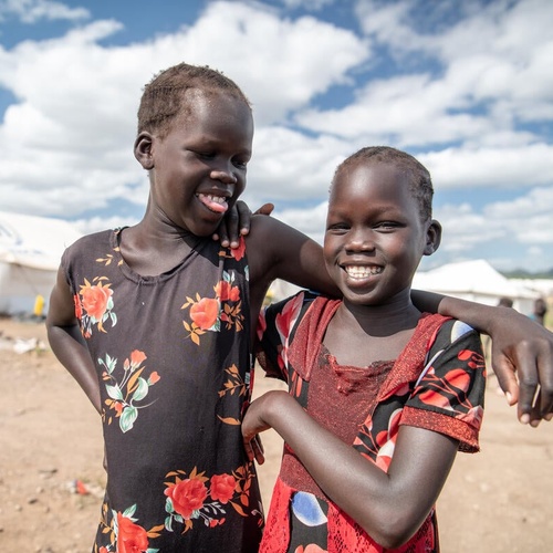 Two sisters laughing, their arms around each other, at the Kalobeyei Reception Center in Kenya