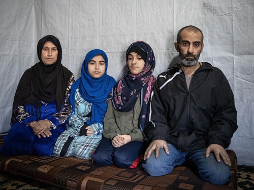 A family of four kneels on the floor inside a tented structure.