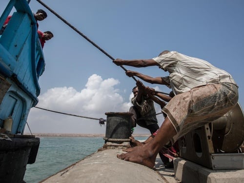 Men pull a rope to bring a boat into dock.