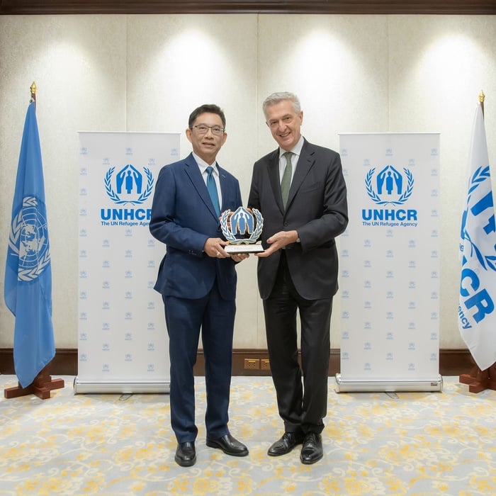 Mr. Wanchai Tachavejnukul and Filippo Grandi smiling and holding an award together, standing in front of UNHCR banners and flags