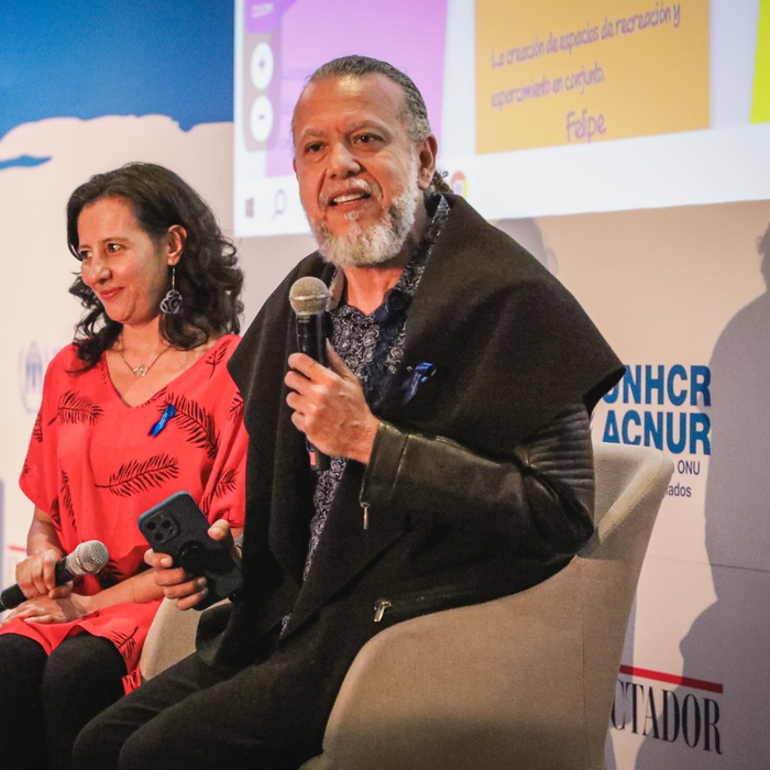 Alberto Dinero on stage talking into a microphone.