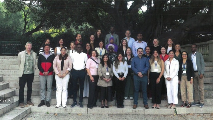 A group of people are standing outside, lined up and smiling into the camera. 