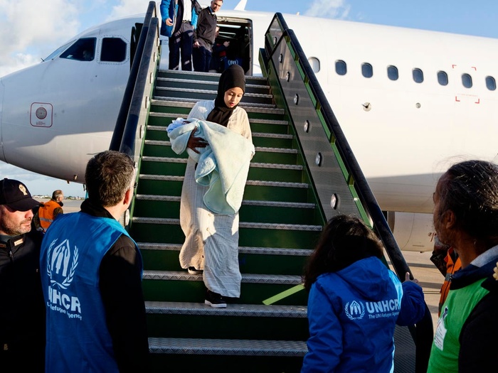 A Somali woman holding a baby is greeted by UNHCR staff as she exits a plane after being evacuated from Libya to Italy. 