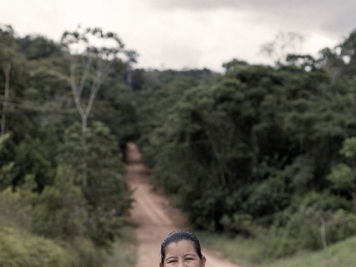 A woman stands in a dirt road that passes through a forest