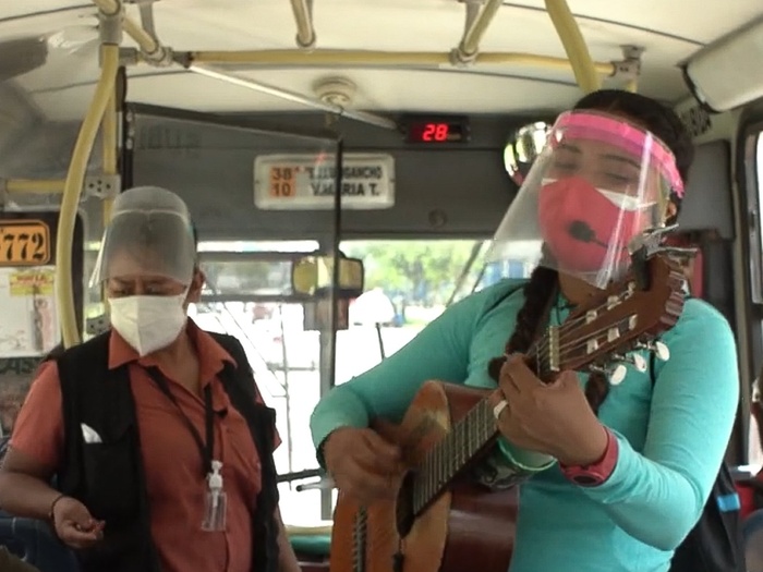 Cristina playing the guitar in a bus, wearing a mask