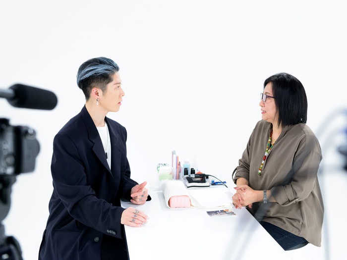 MIYAVI pictured in a nail salon, speaking to a nail artist, while a video camera films.
