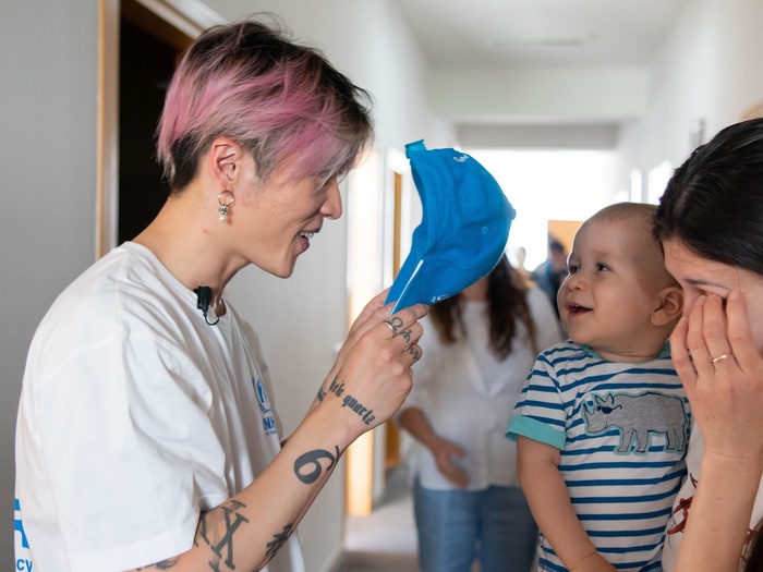 MIYAVI plays peek-a-boo behind his hat with a baby held by its mother.