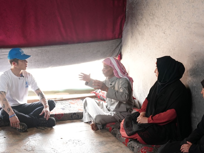 MIYAVI sits on the floor, deep in conversation with three refugees.