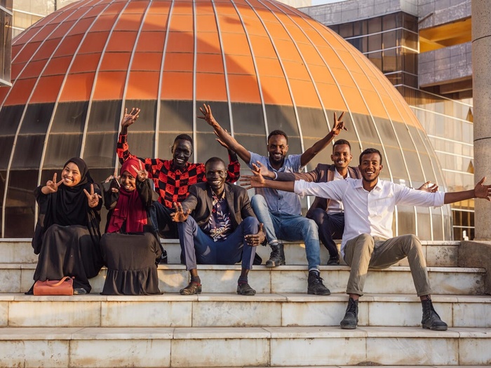 A group of young women and men, sitting on the stairs in front of their university.
