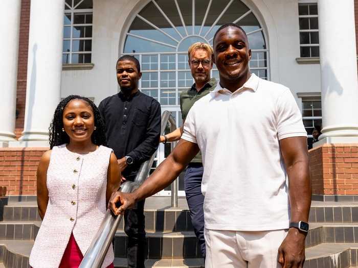 Emmanuel Tshituka, a 25-year-old man, is pictured smiling on a set of stairs, a woman beside him and two men behind them.