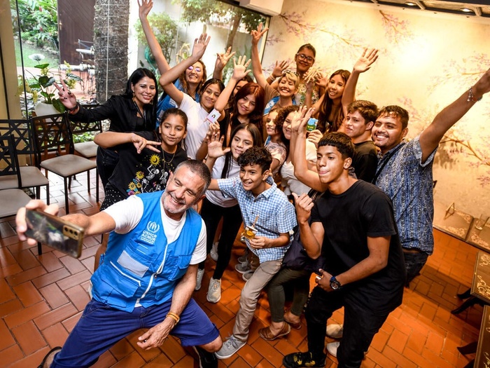 Osvaldo Laport in a UNHCR vest takes a selfie with a large group of smiling refugee youth.