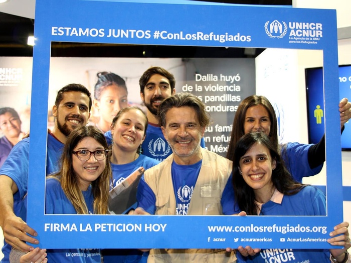 A group of people in UNHCR branding hold up a photo frame around them which says "Estamos juntos #ConLosRefugiados" and "Firma la petition hoy"