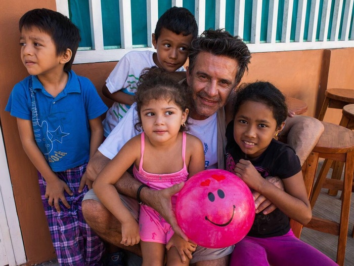 Osvaldo Laport pictured with four asylum-seeker children, holding a pink ball with a smiley face on it.