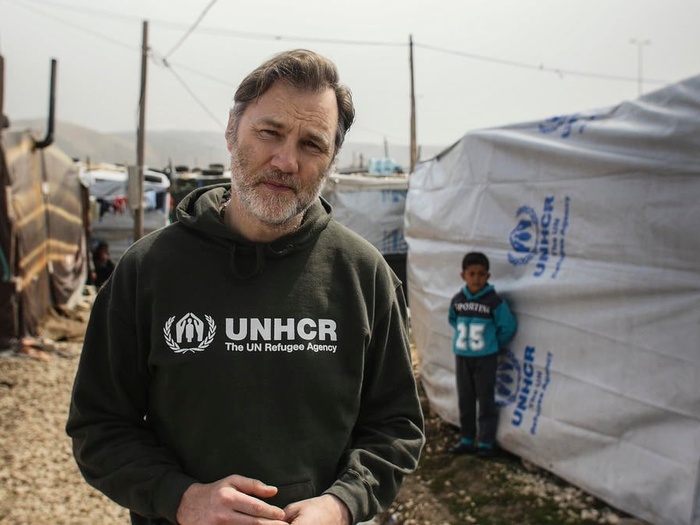 David Morrissey stands in front of a UNHCR tent.