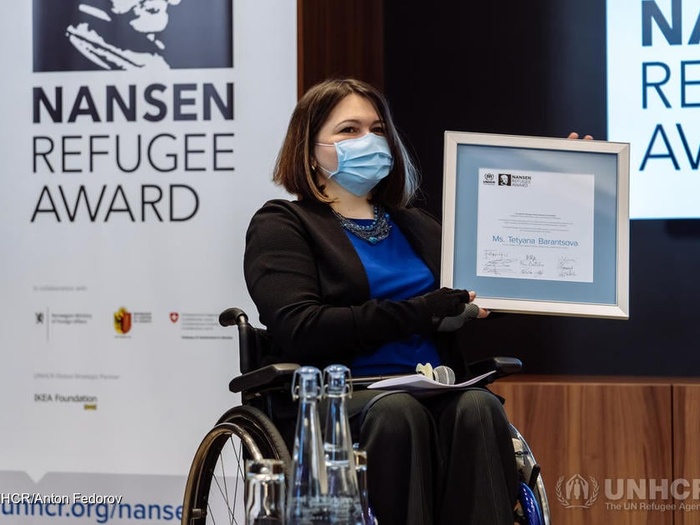 A woman in a wheelchair holds the Nansen refugee regional award.