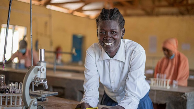 A young woman in a science classroom smiles for the camera. 