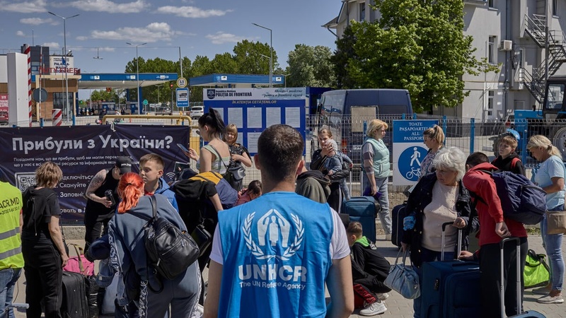 A UNHCR staff member provides assistance to a large group of Ukrainian refugees, who gather with their belongings in Moldova after crossing the border.