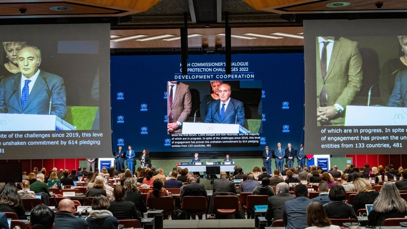 Three large screens show a projection of a speaker in a huge conference room.