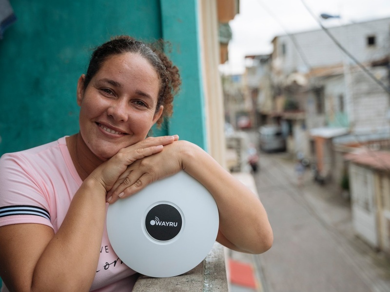 A woman leans on a Wi-Fi router on a balcony overlooking a street.