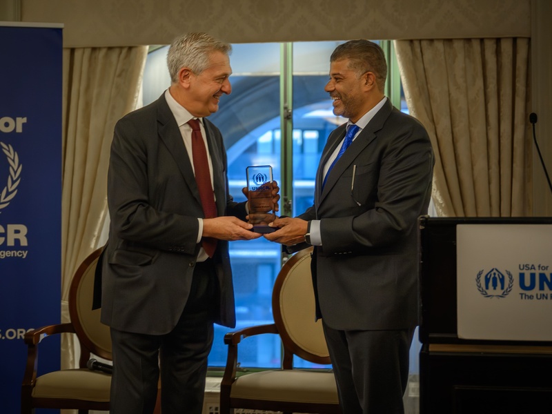 Two men pose for the picture, holding a small glass certificate with the UNHCR logo.
