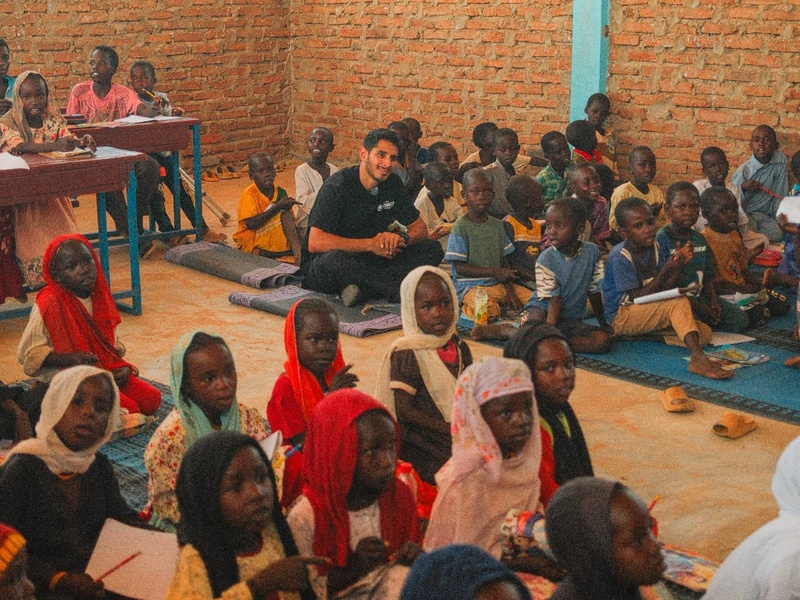 Omar sitting on the ground in a classroom together with young students