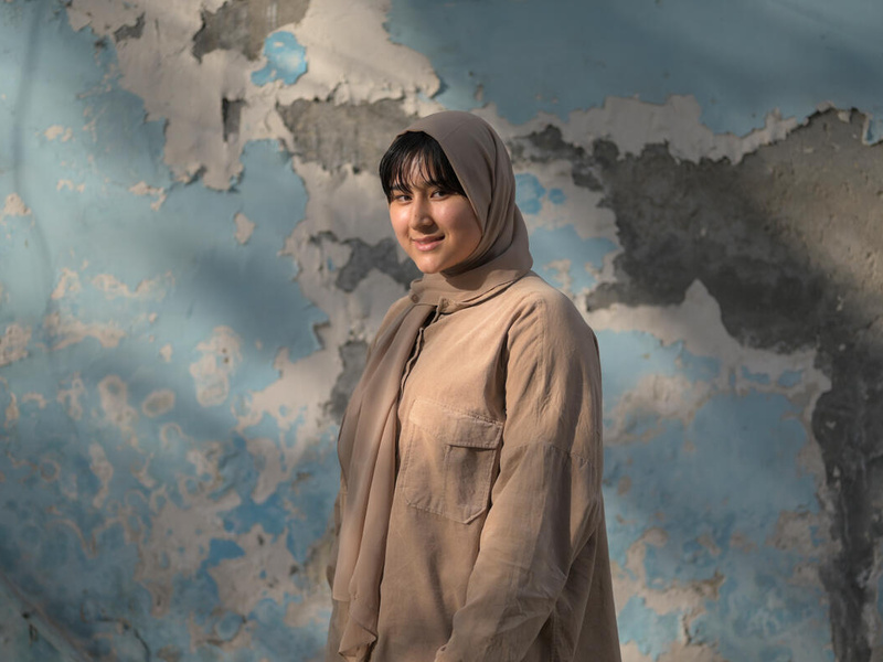 Afghan refugee woman stands in front of a blue wall.