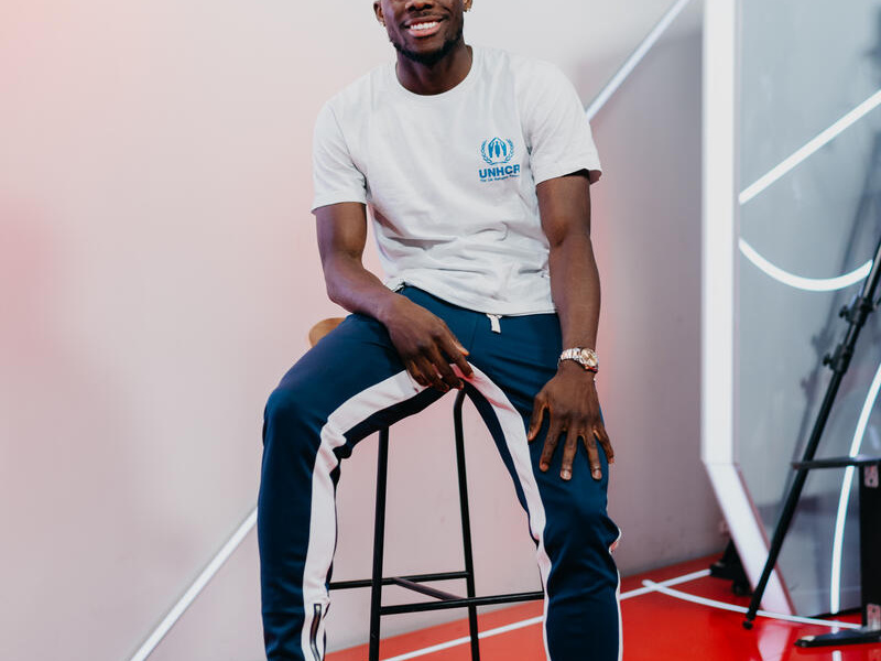 Alphonso Davies sits on a chair, a soccer ball under his foot.