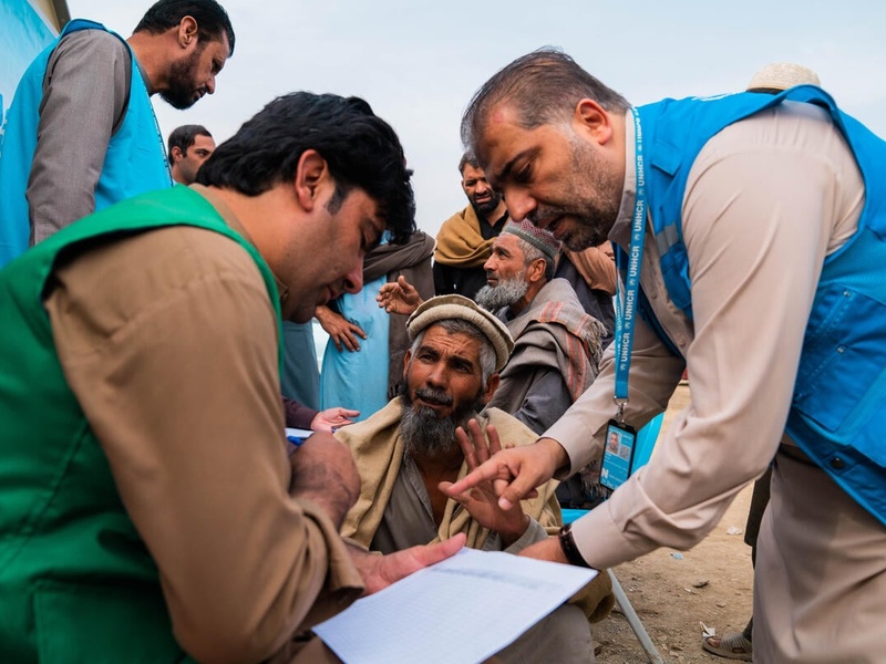 UNHCR staff members discuss with a group of men and look together at a document.