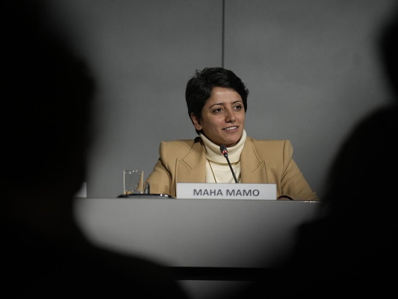 Formally stateless person Maha Mamo speaks at a panel during the Global Refugee Forum 2023. She is seated at a table, with the silhouettes of audience members framing the scene.