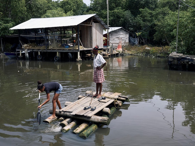 Two girls paddle across mangrove canal on a makeshift wooden raft