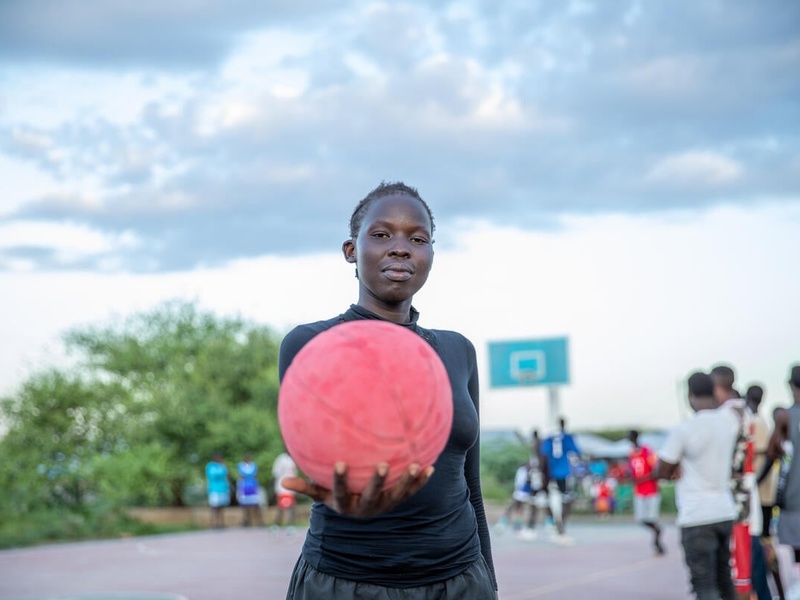 A young girl confidently holds a pink basketball toward the camera.