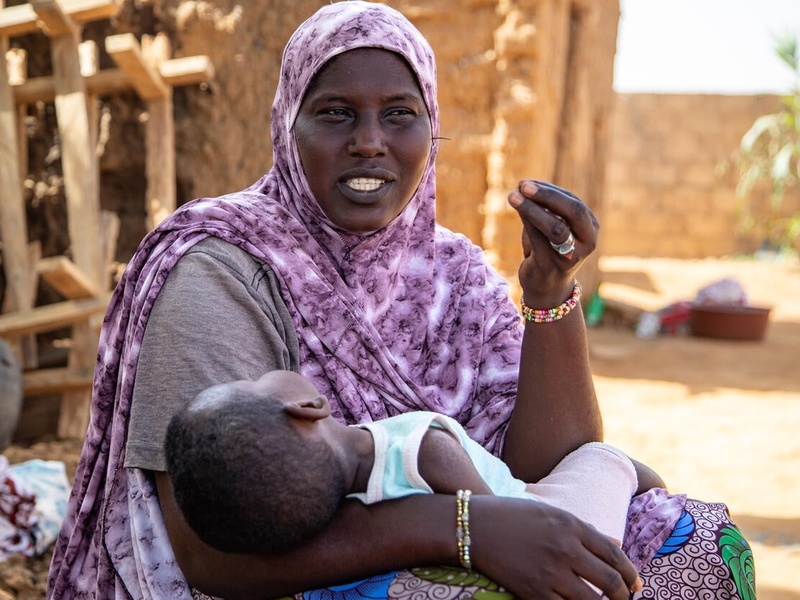 A woman in a purple headscarf holding her sleeping child.