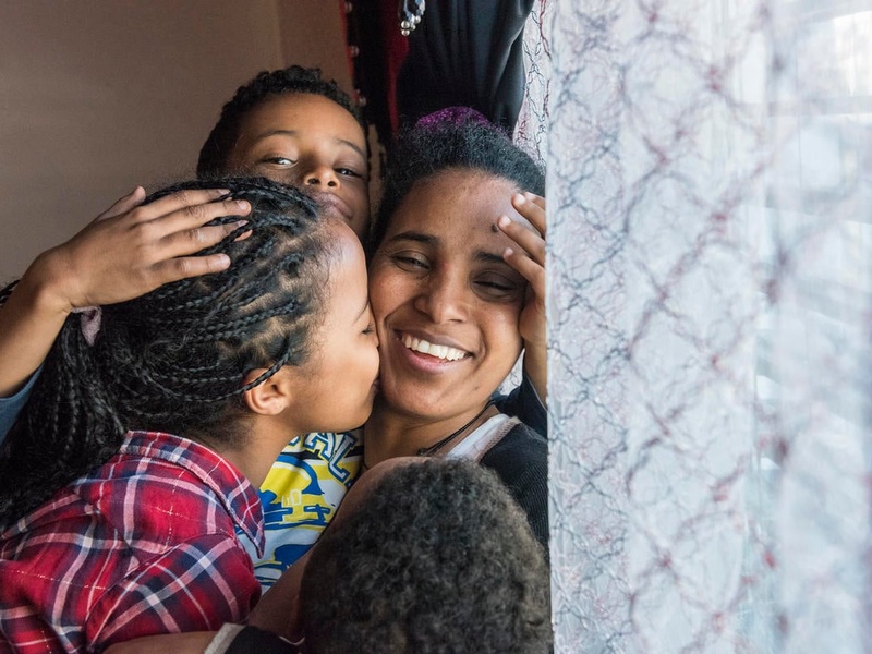 A woman smiles while hugging her three children.