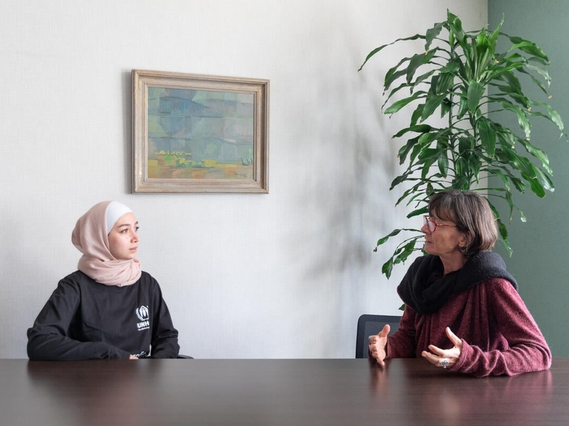 Two women sit together at a table and talk.