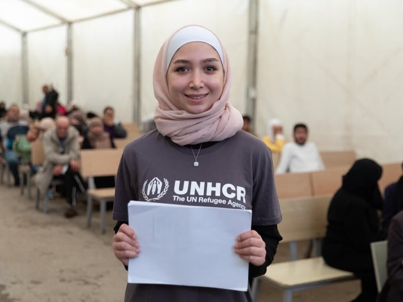 A young woman stands in a waiting room, holding documents in her hands.