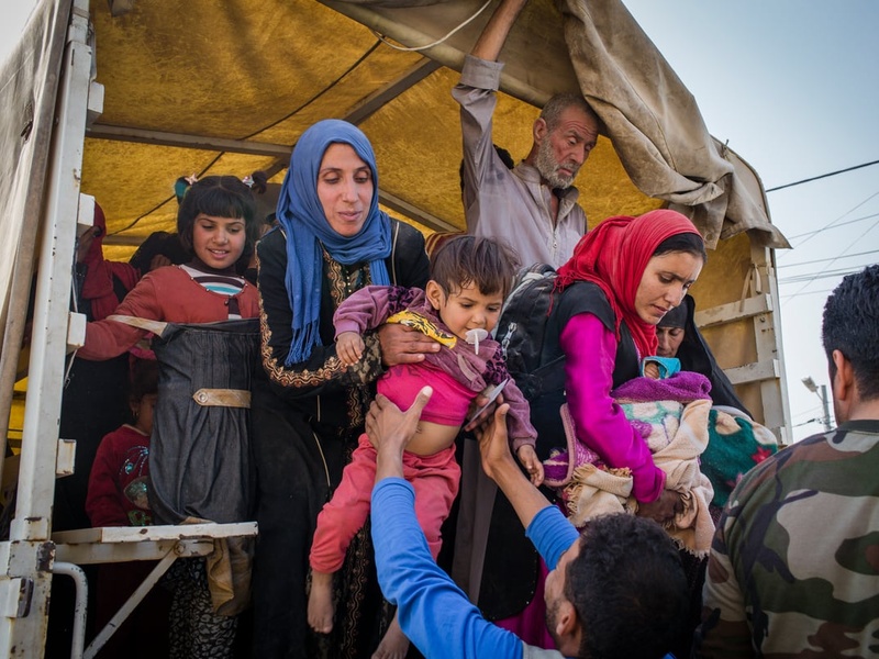 Iraqi men, women and children climbing down from a truck