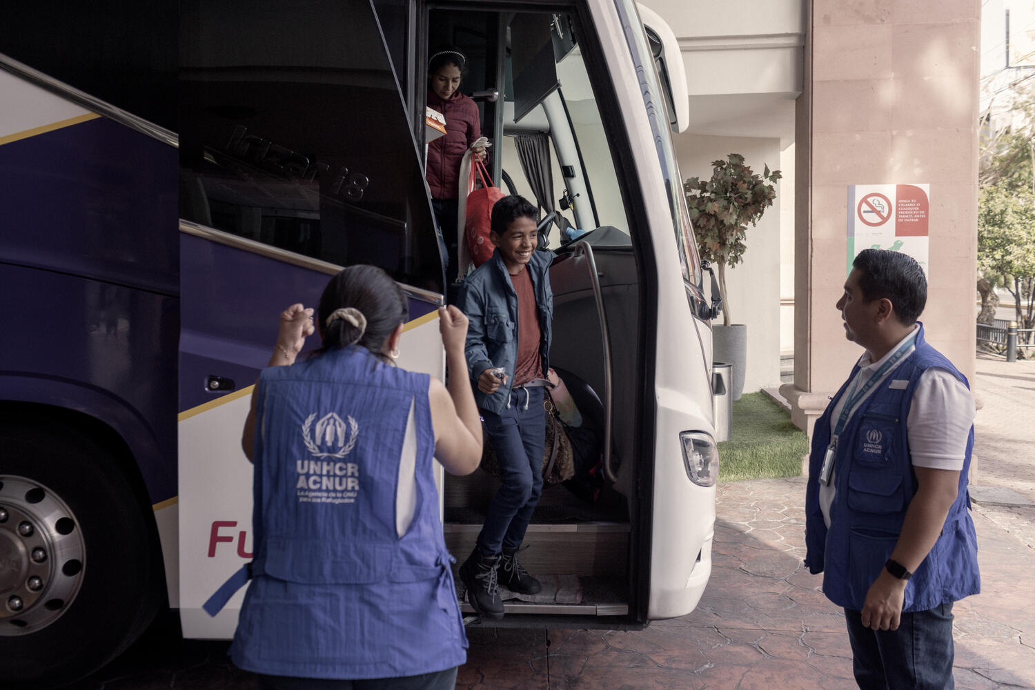 A boy is greeted by UNHCR staff as he steps off a bus.