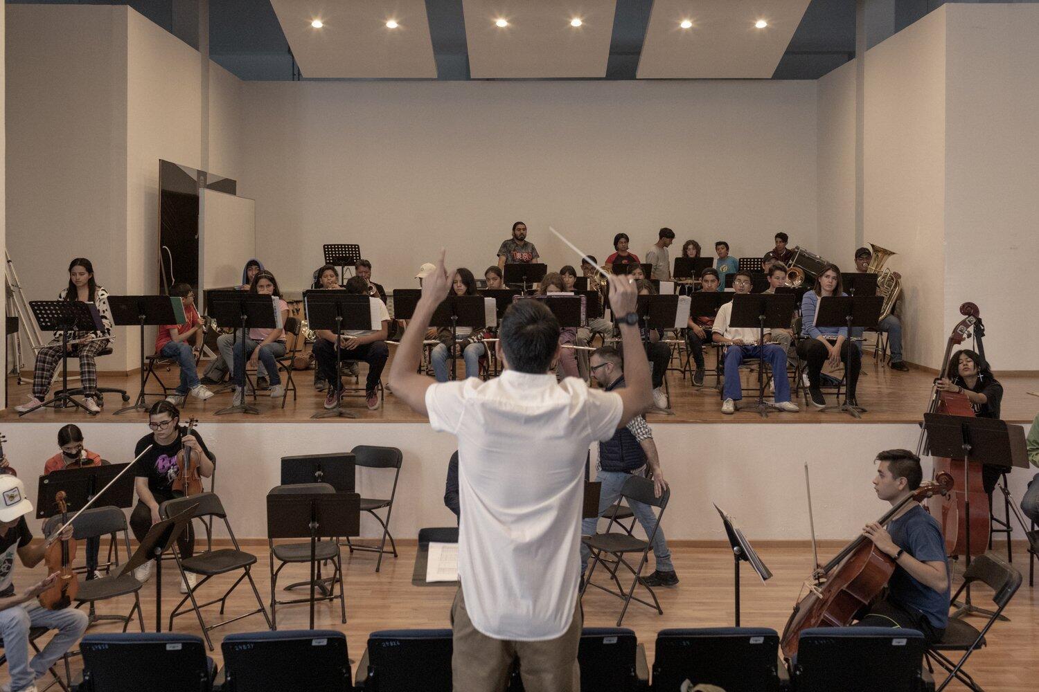 A man conducts an orchestra as they rehearse.