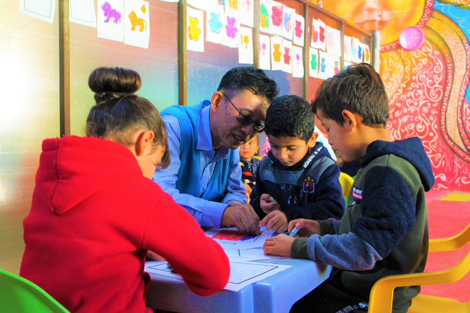 Mr. Wanchai Tachavejnukul sitting at a table, surrounded by children.