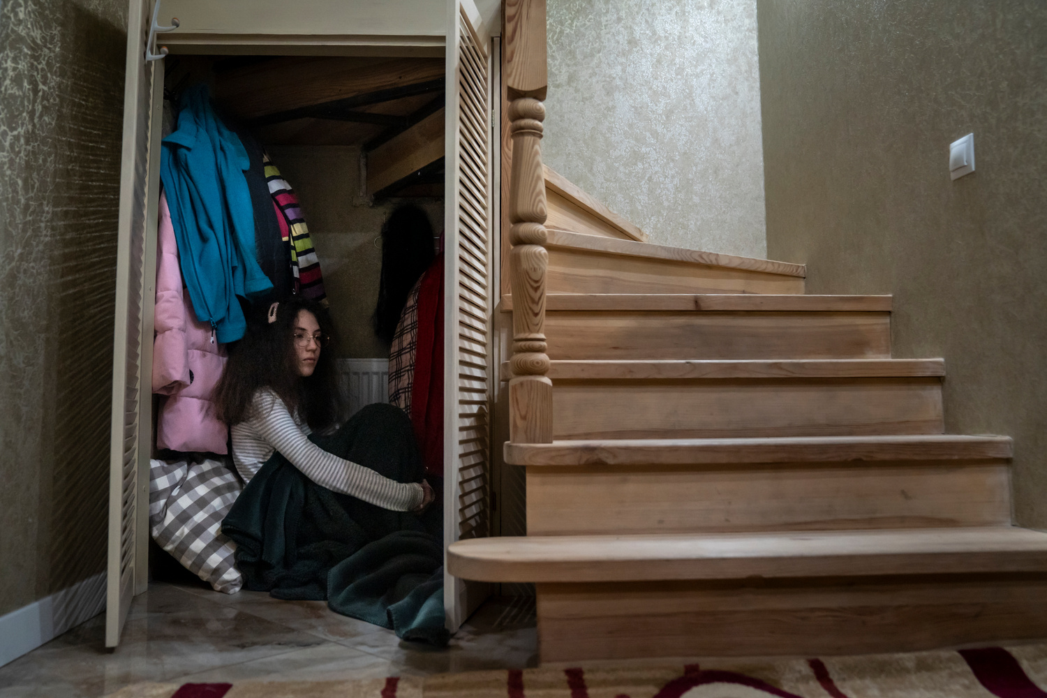 A girl sits in a cupboard under the staircase of her home.