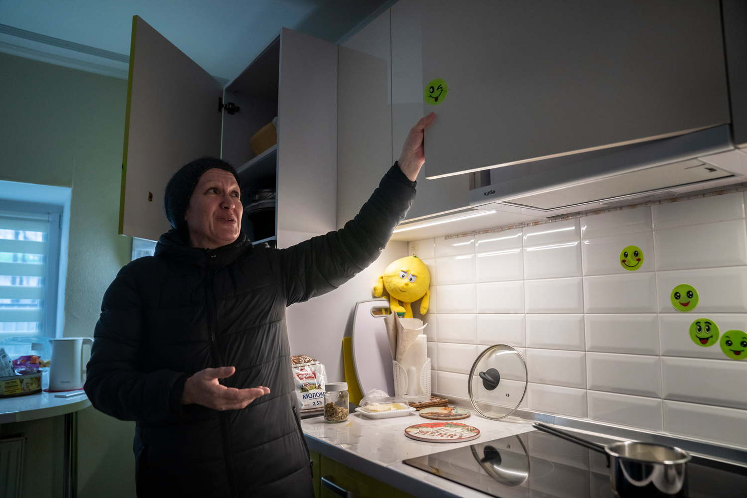 A woman points to stickers covering shrapnel damage in the kitch of her home.