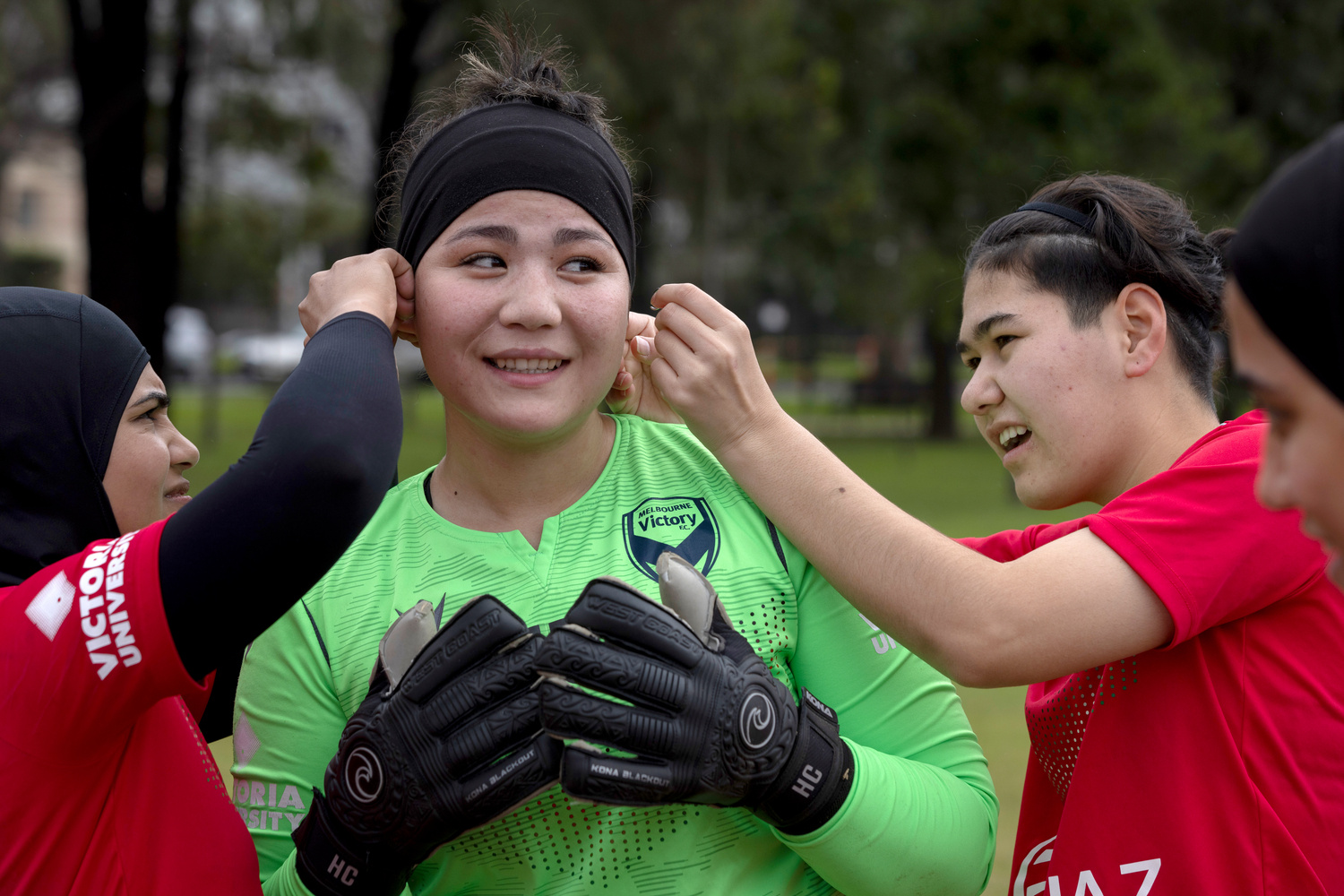 Two girls dressed in football jerseys help their teammate adjust her hair band.