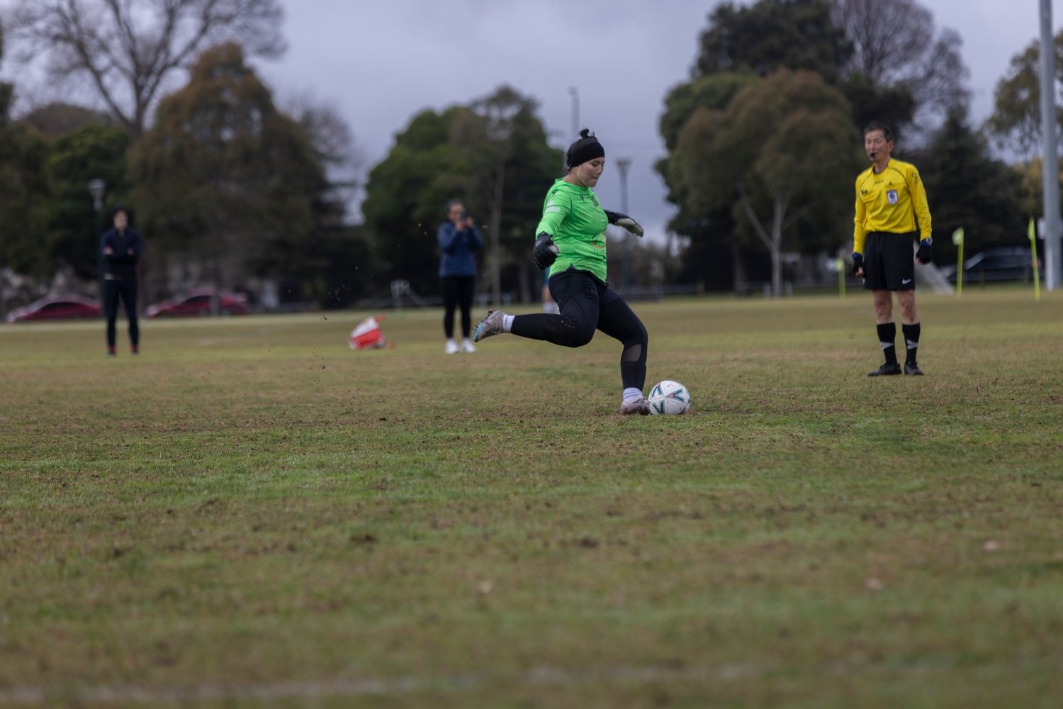 A young woman in a green jersey is about to kick a football.