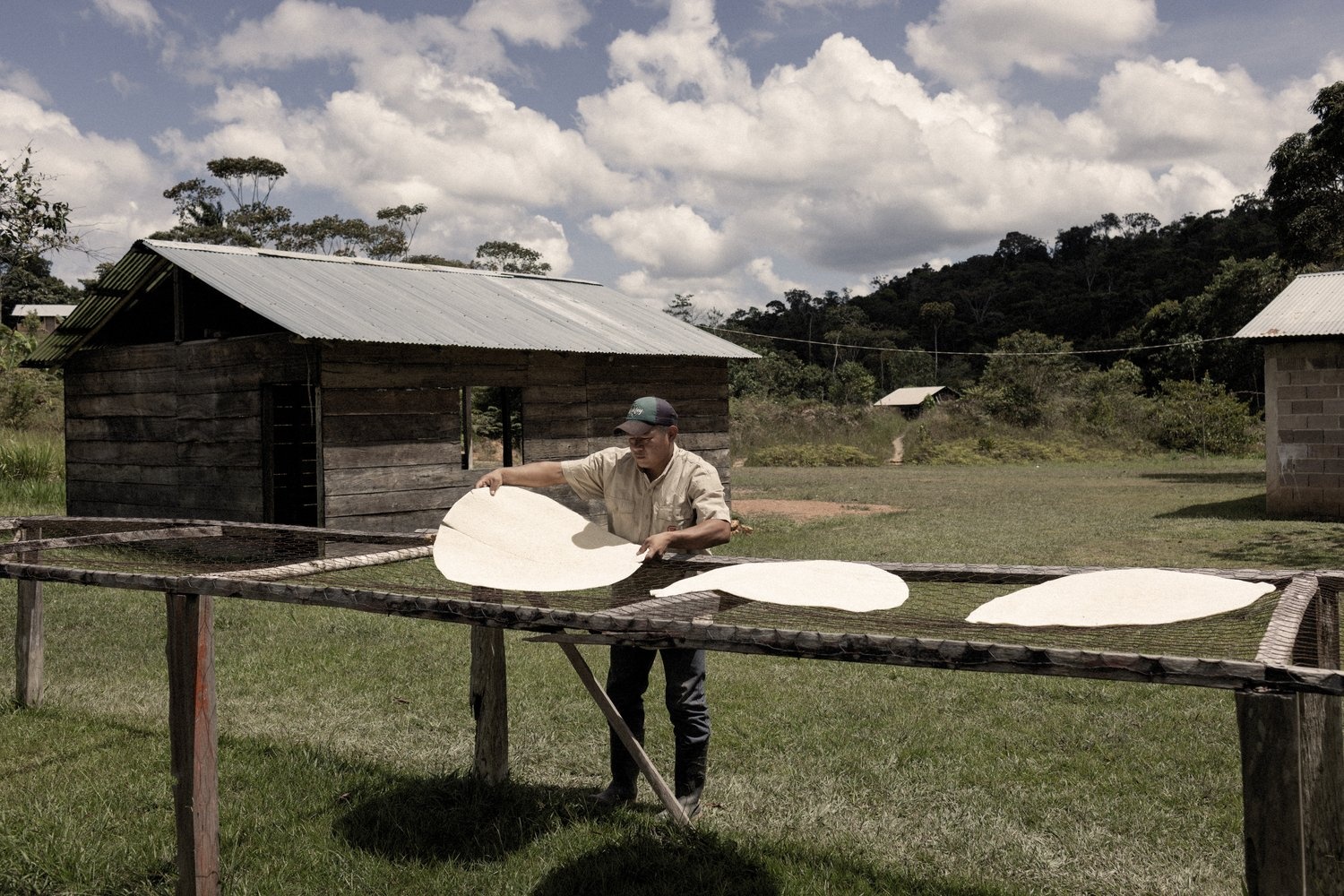 A man flips large flatbreads drying outside on a wood and wire rack.