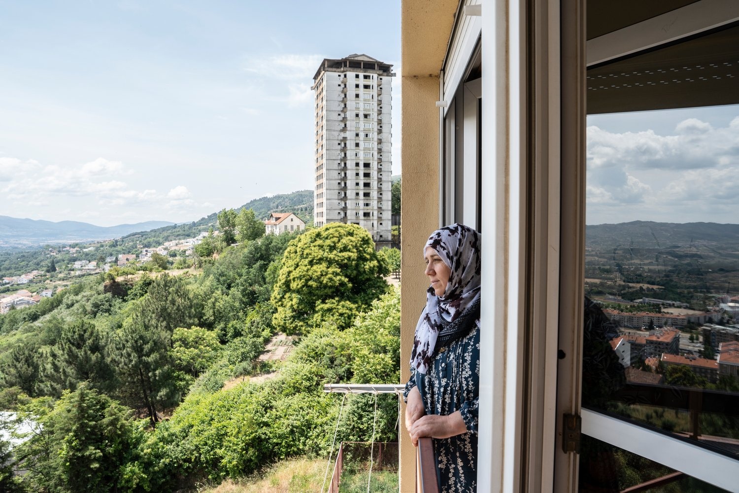A woman looks out of the window of a high-rise building.