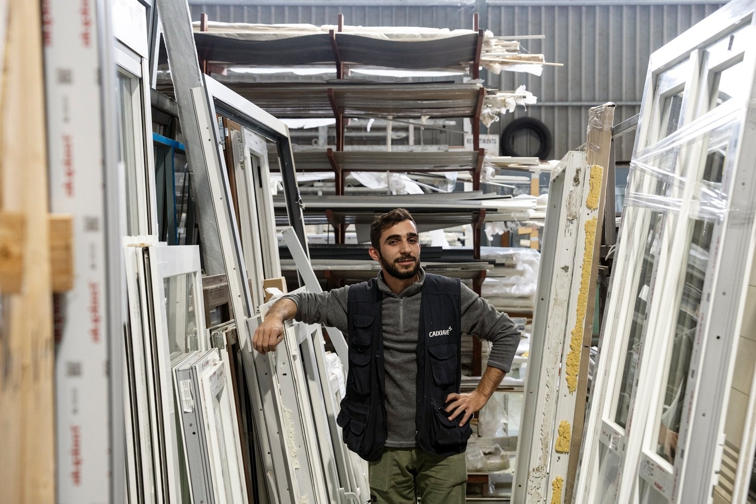 A young man leans his arm on window frames on the floor of a factory.
